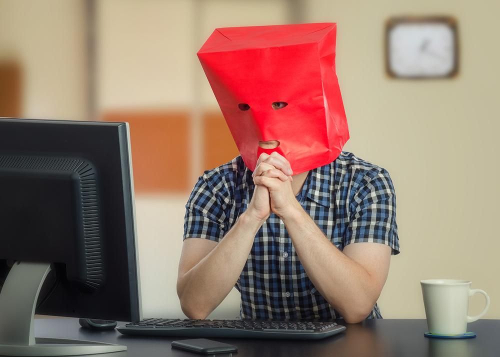 Kockás inges férfi ül a monitor előtt piros papírtáskával a fején