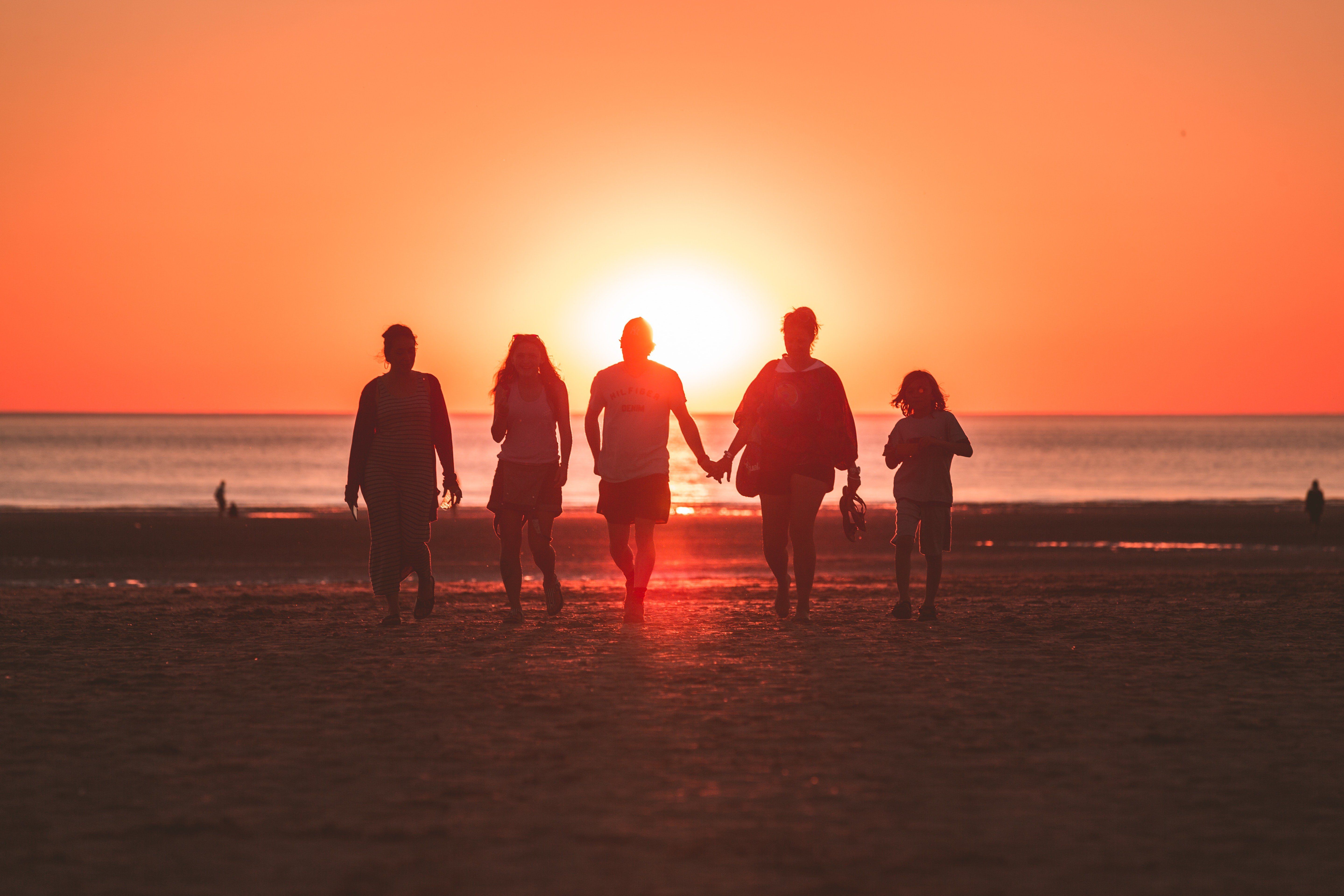 Tengerparton sétáló család naplementében