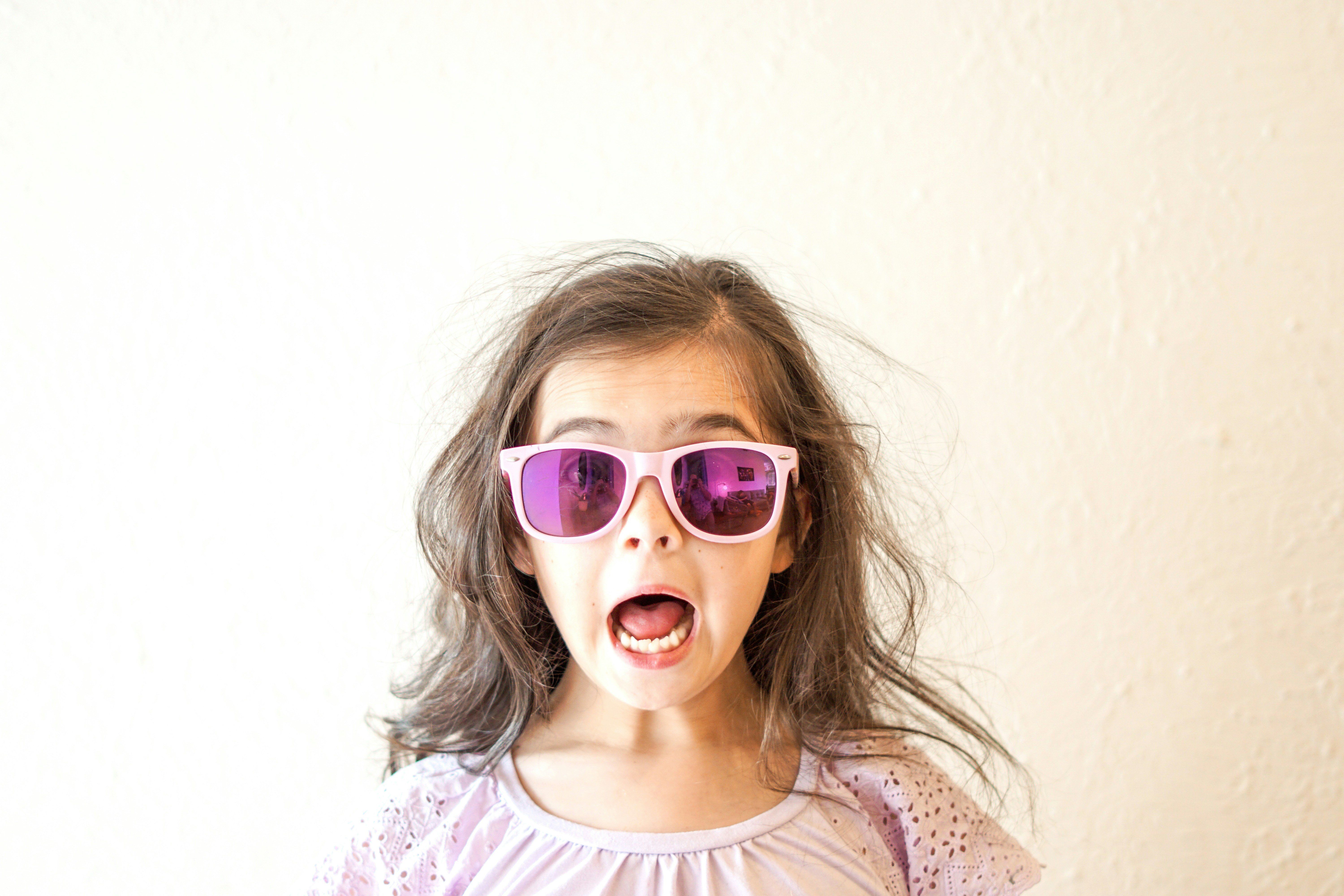 Tátott szájjal csodálkozó napszemüveges kislány
