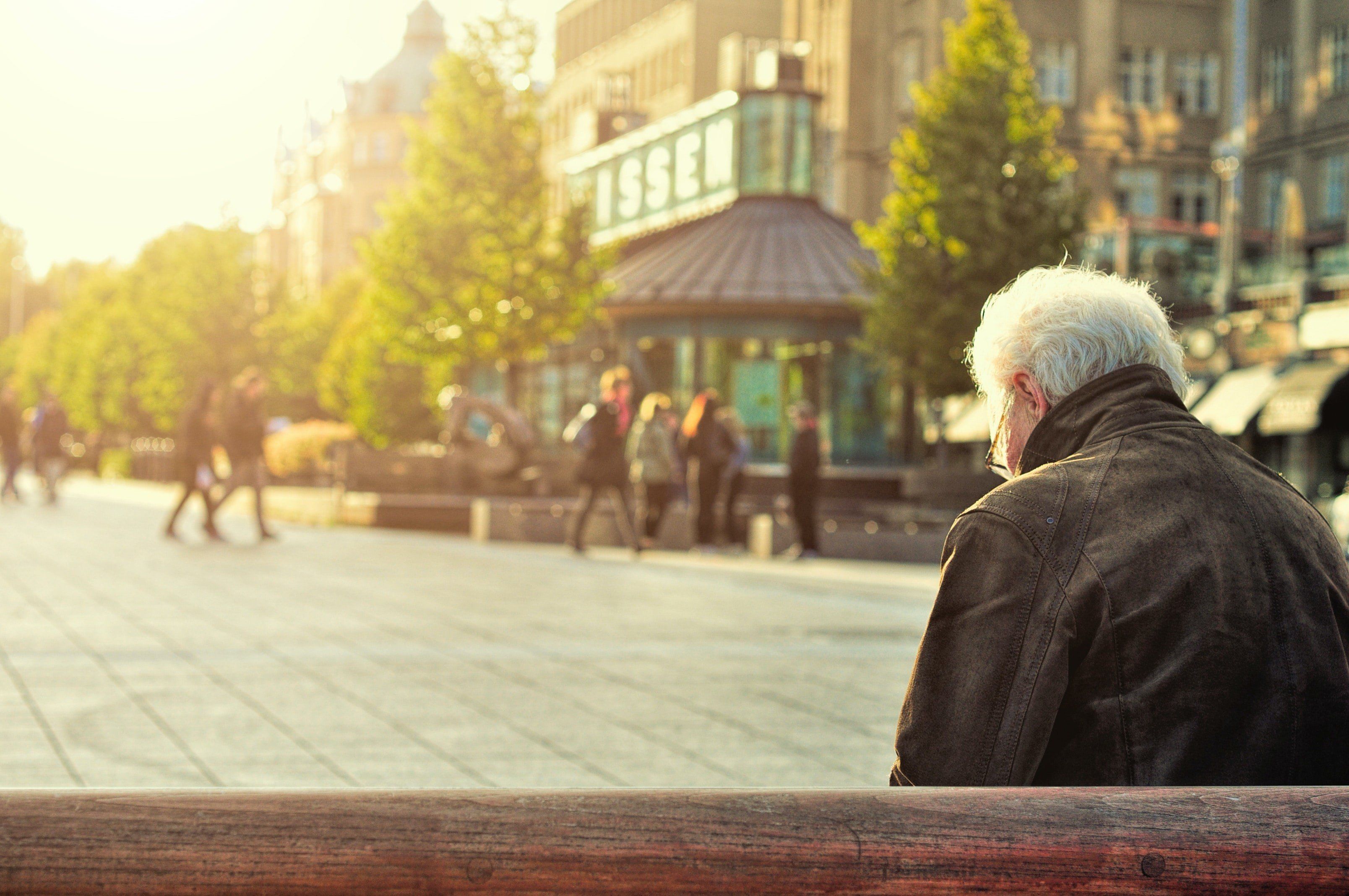 Nyugdíjas hátulról fényképezve üldögél egy belvárosi padon