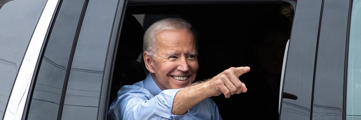 Joe Biden egy autóban mosolyog, lehúzott ablakból integet