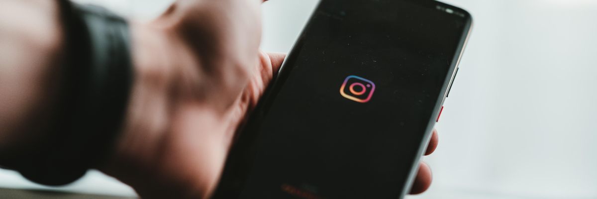 Karórás férfi a kezében tartja telefonját, melynek képernyőjén az Instagram logója látható