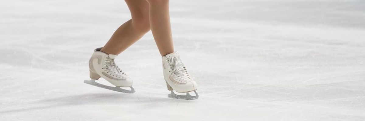 Kék ruhás, fehér korcsolyás műkorcsolyázó korcsolyázik a 2022-es pekingi téli olimpián