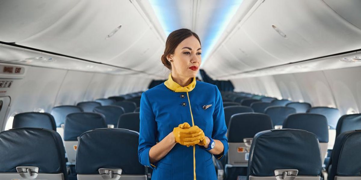 Kék-sárga munkaruhás légiutaskísérő nézelődik az üres repülőgép utasterében