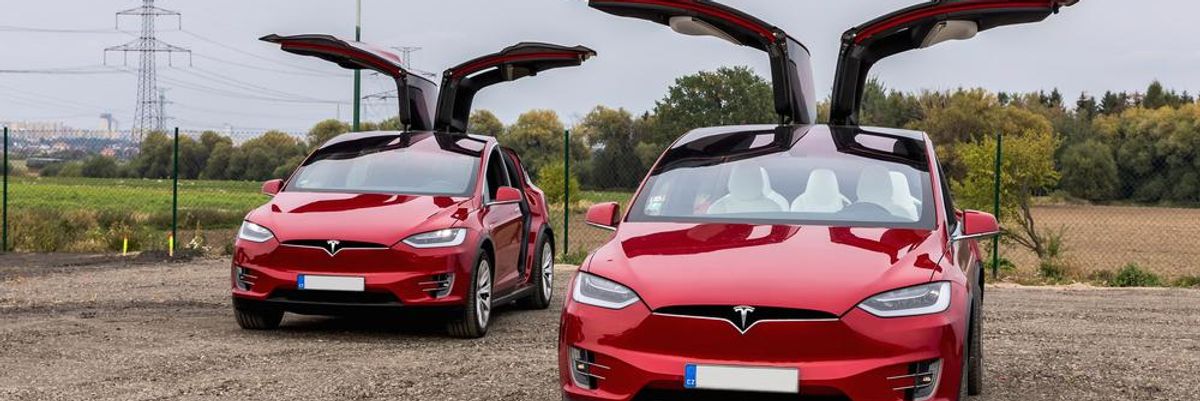 Két piros Tesla Model X áll egymás mellett nyitott ajtókkal, ezek az autók is érintettek a visszahívásban