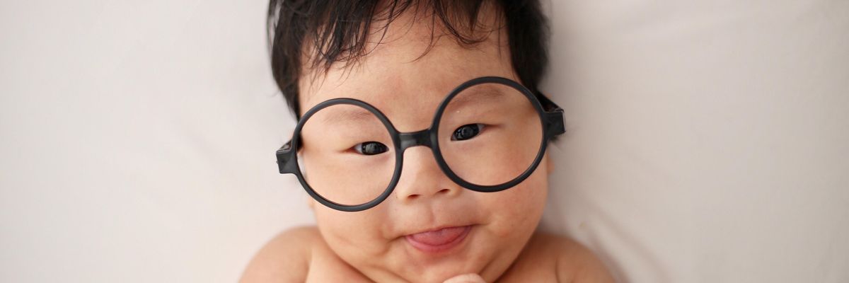 Kína csecsemő szemüvegben mosolyog egy fehér lepedőn
