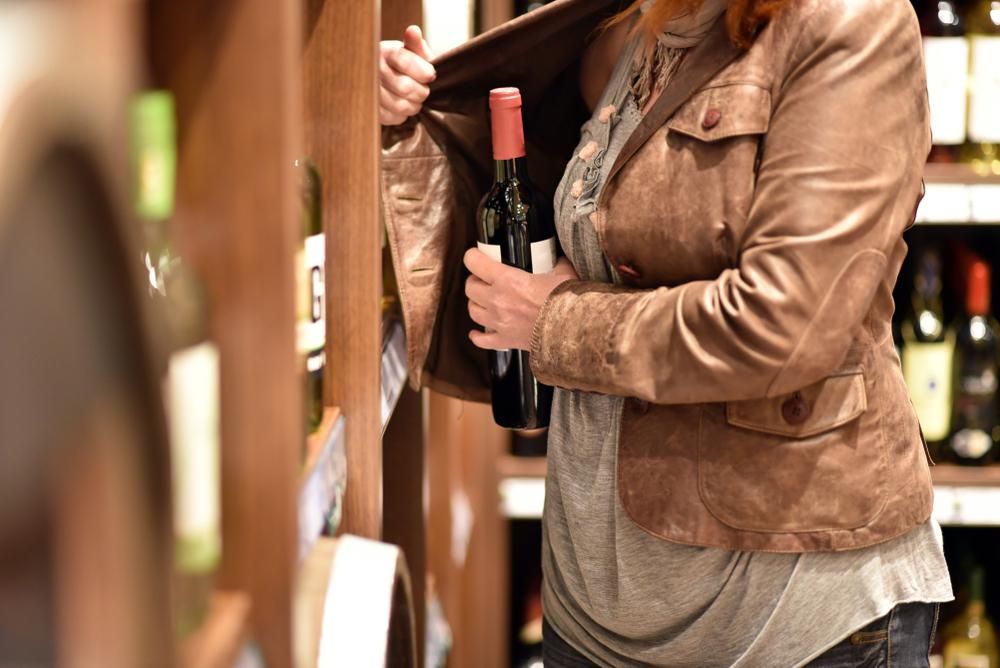Egy nő egy üveg bort készül ellopni a kabátja alá rejtve egy élelmiszerboltban 