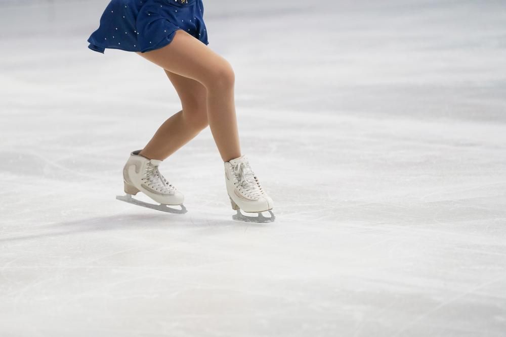 Kék ruhás, fehér korcsolyás műkorcsolyázó korcsolyázik a 2022-es pekingi téli olimpián
