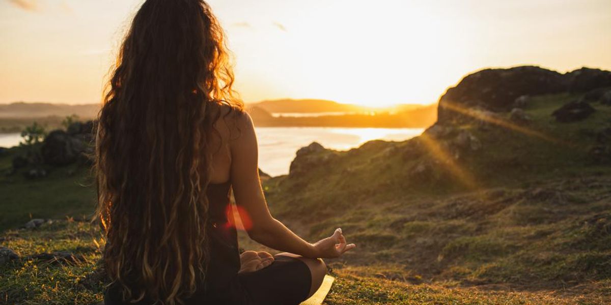 Melírozott hajú lány meditál egy tengerparton a naplementében egy pénteki napon, ugyanis a munkahelyén csupán négy napot kell dolgoznia egy héten, ezért pénteken is meditálhat