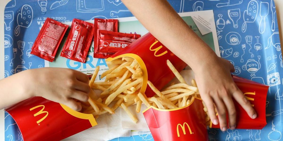 Négy közepes adag McDonald's-os sült krumpliból falatozik két ember, a krumplik egy kék tálcán vannak, amelyen négy ketchup is található