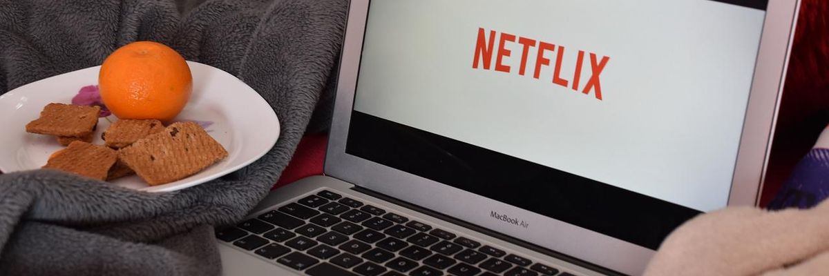 Netflixet néz valaki egy laptopon, ami az ágyon van, mellette egy tányér, amiben narancs és kekszek vannak