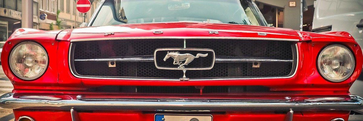 Piros Ford Mustang áll a parkolóban házak között nappal