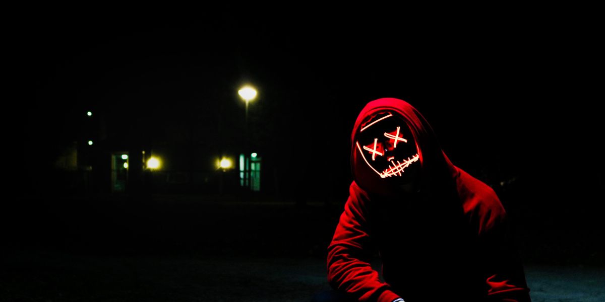 Piros pulcsis hacker guggol a sötét utcán egy világító maszkban