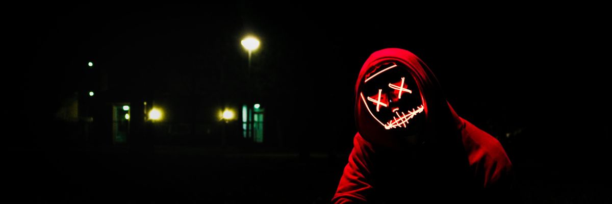 Piros pulóveres hacker guggol éjszaka az utcán, egy pirosan világító maszk van az arcán