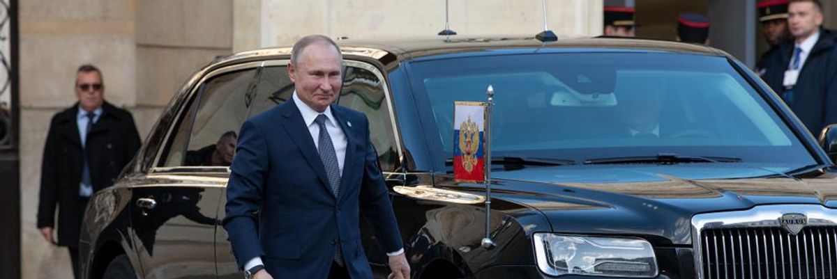 Putyin elnök egy páncélozott  autó mellett sétál, magabiztos léptekkel