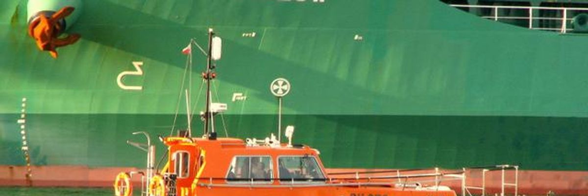 Révkalauz piros motorcsónakkal közelíti a zöld konténerhajót