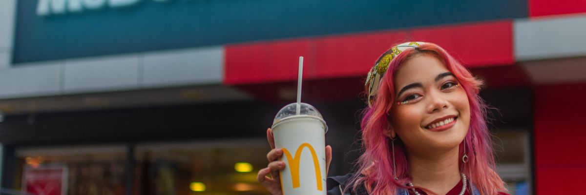 Rózsaszín hajú, mosolygós ázsiai lány egy McDonald's-os shake-et tart a kezében egy Meki étterem előtt