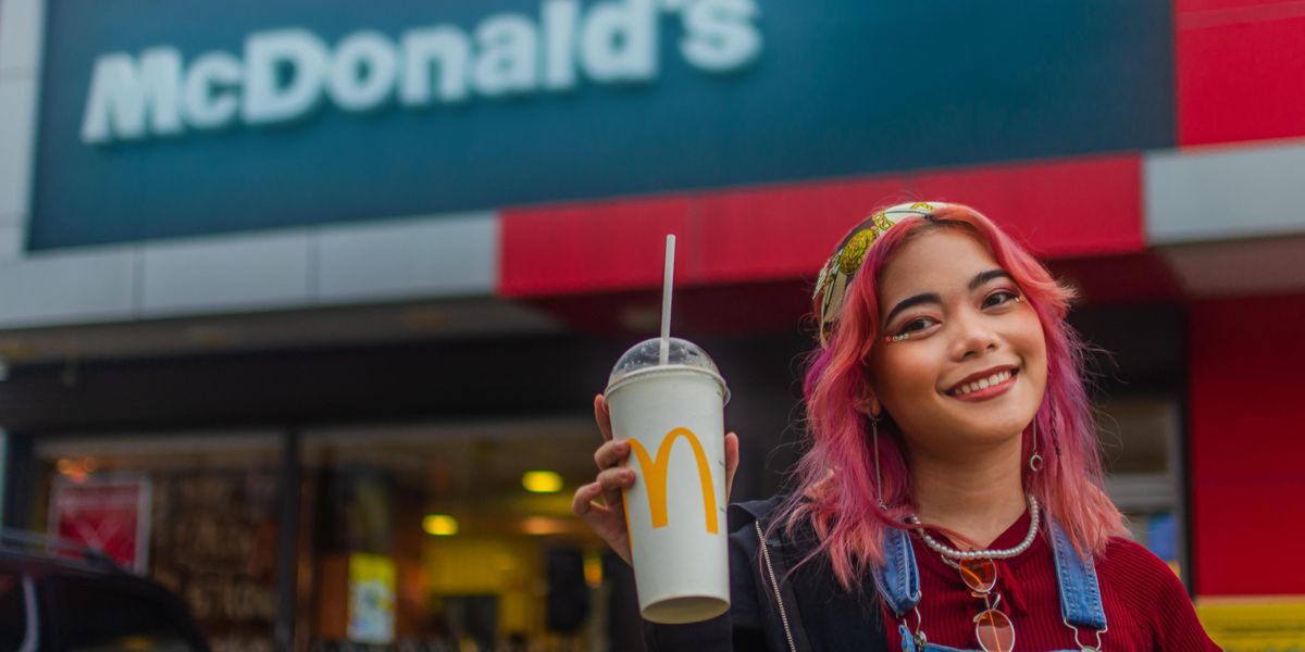 Rózsaszín hajú, mosolygós ázsiai lány egy McDonald's-os shake-et tart a kezében egy Meki étterem előtt