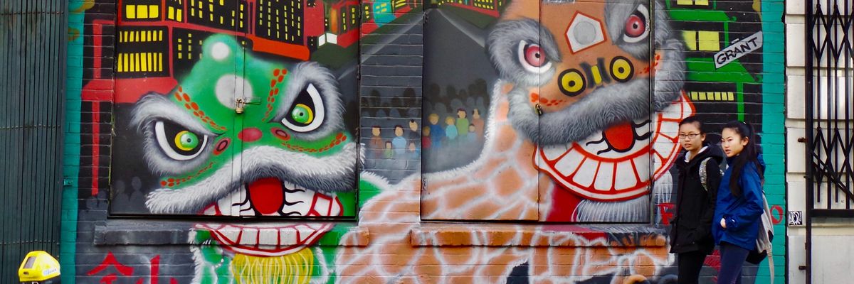 San Francisco Kínai Negyedében ázsiai lányok sétálnak sárkányos graffitik előtt