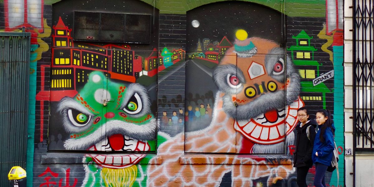 San Francisco Kínai Negyedében ázsiai lányok sétálnak sárkányos graffitik előtt