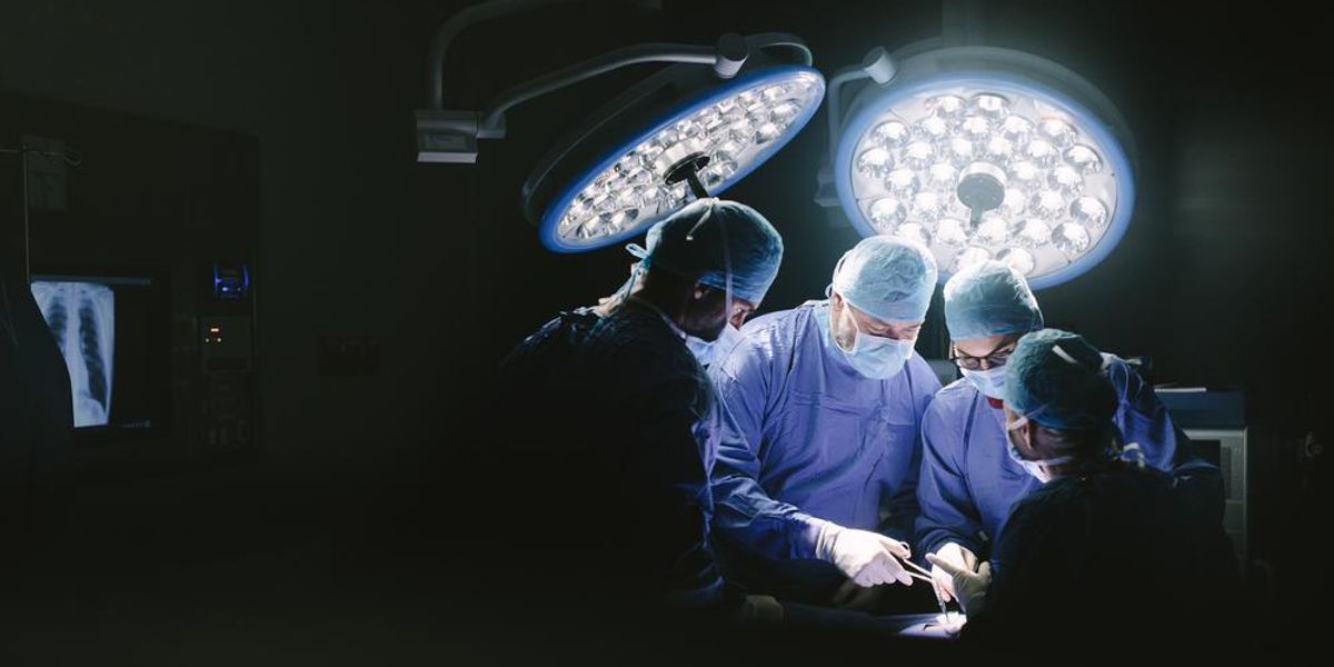 Sebészek műtenek egy embert a műtőszobában nagy teljesítményű lámpák alatt maszkban, kék orvosi köpenyben