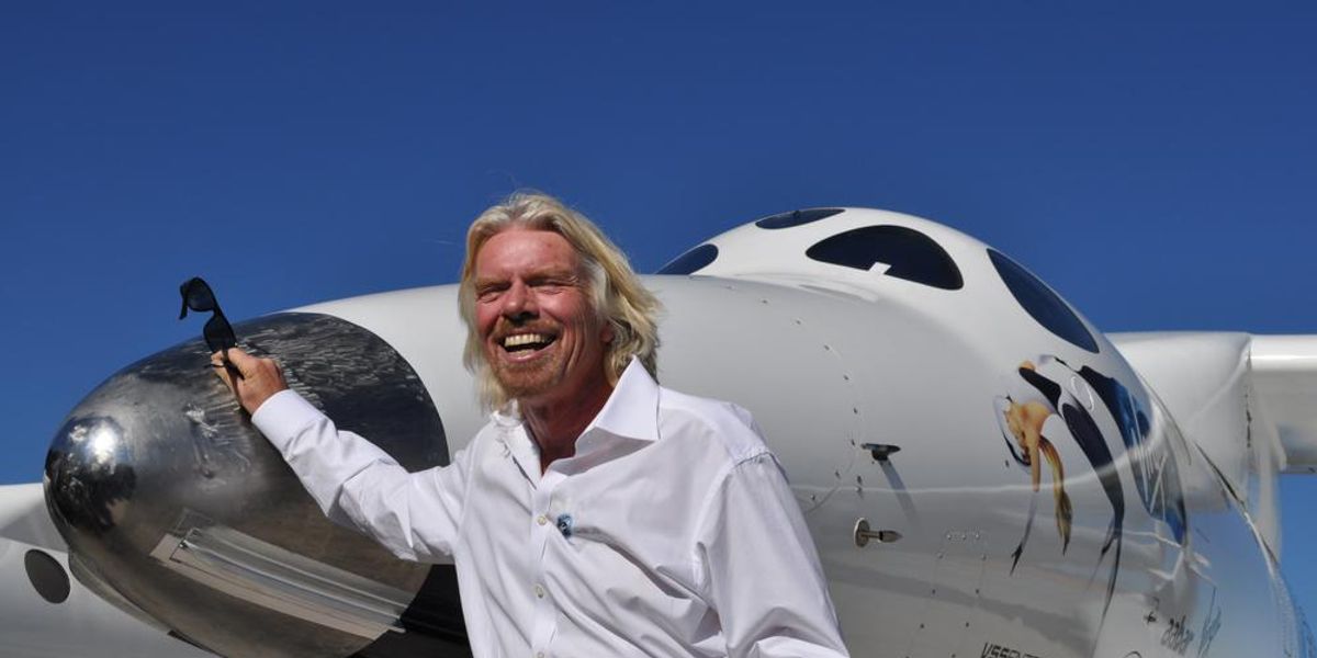 Sir Richard Branson fehér ingben nevet a VSS Enterprise űrhajó előtt