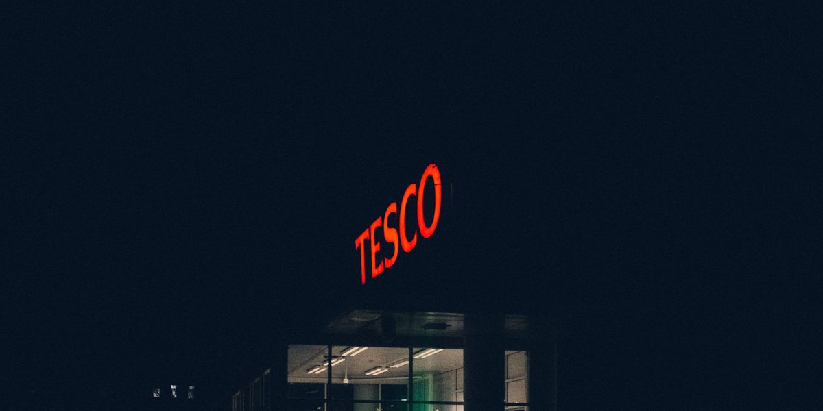 Sötétben pirosan világító Tesco felirat egy áruház tetején