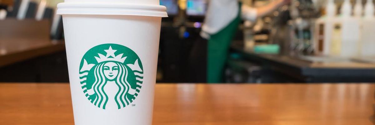 Starbucksos kávéspohár a cég logójával a kávélánc egyik üzletében, a háttérben egy barista dolgozik