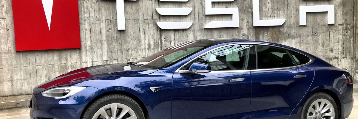 Tesla logo előtt egy kék Tesla autó
