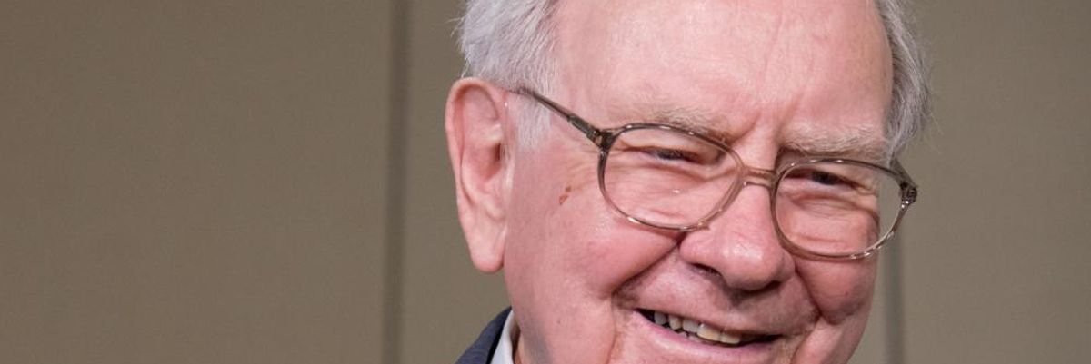 Warren Buffett öltönyben mosolyog a kamerába egy világos fal előtt